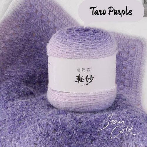 Ball of yarn labeled 'Taro Purple' on a textured purple fabric background