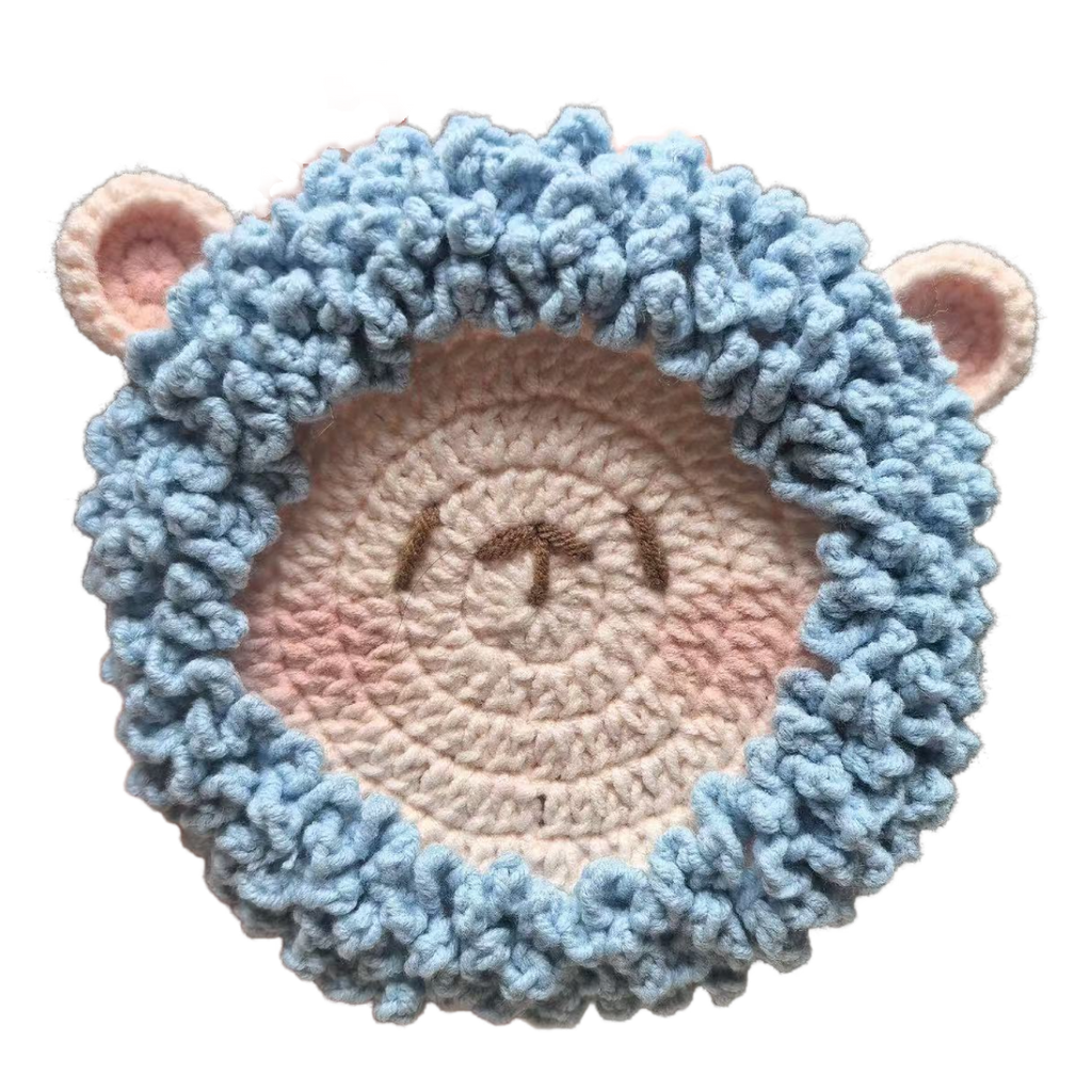 Crocheted sheep face with blue ears and pink nose on a white background