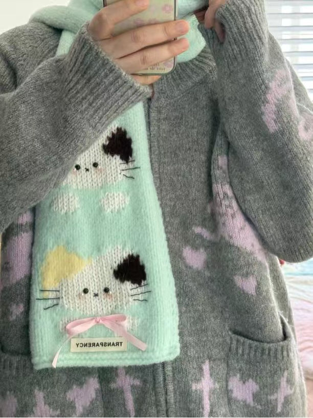 Person wearing a gray sweater holding a light blue knitted scarf with cat designs.