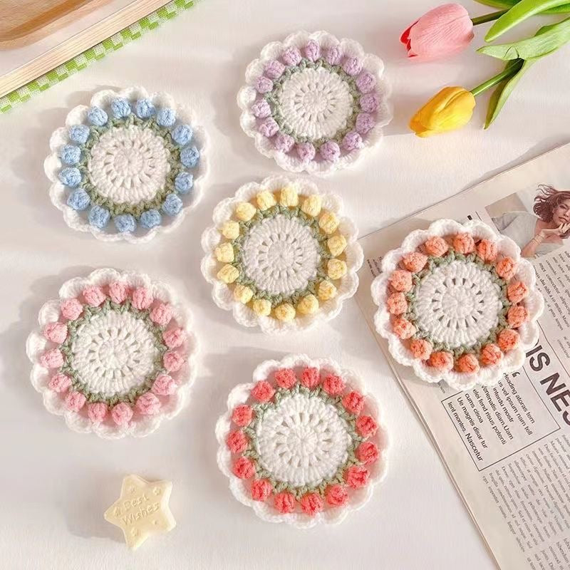 Set of six crocheted coasters with floral patterns on a newspaper and tulips background.