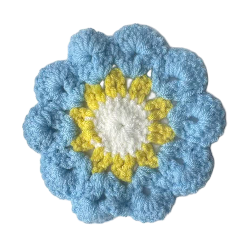 Crocheted flower with blue outer petals, yellow center, and white inner core on a white background