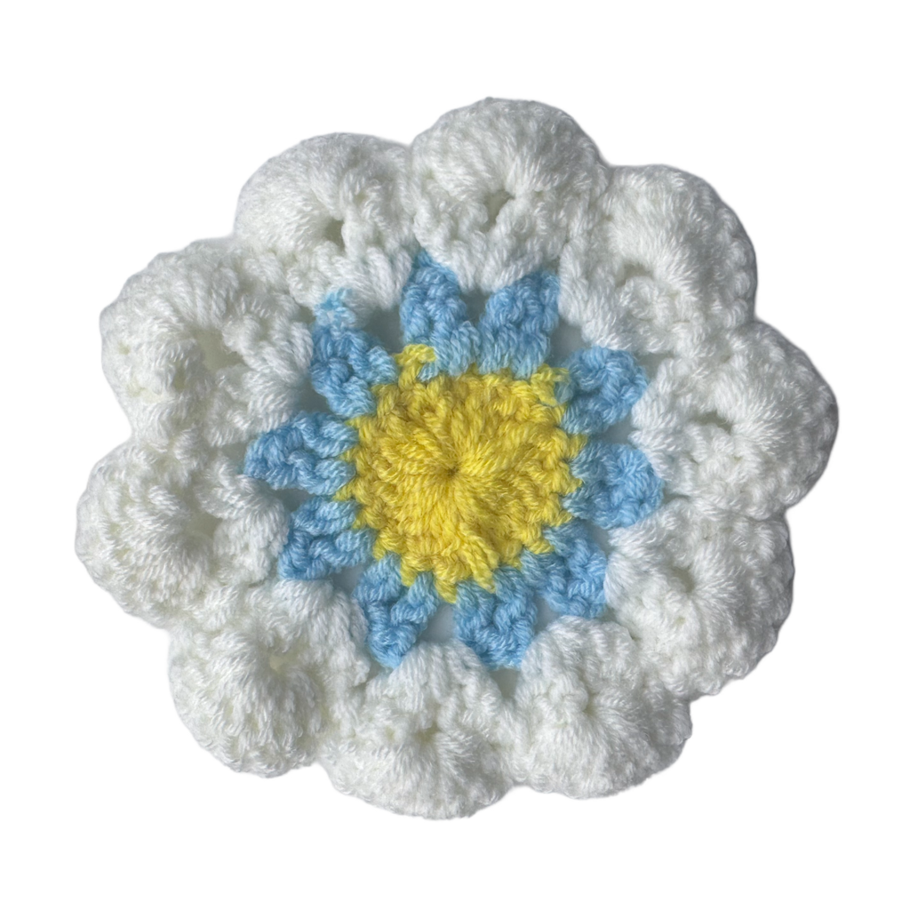 Crocheted flower with white outer petals, blue middle petals, and yellow center on a white background