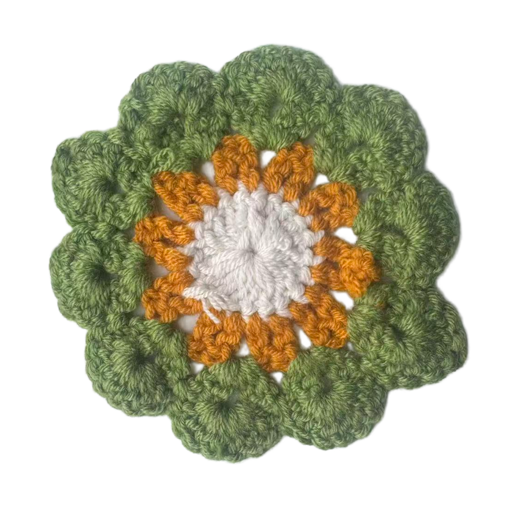 Crocheted flower pattern with green outer petals and orange and white center on a white background