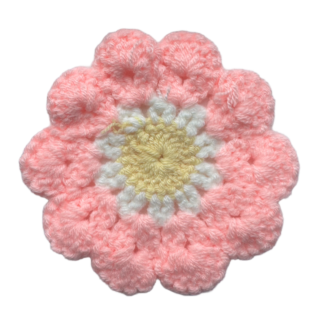 Pink crocheted flower with a yellow center on a white background