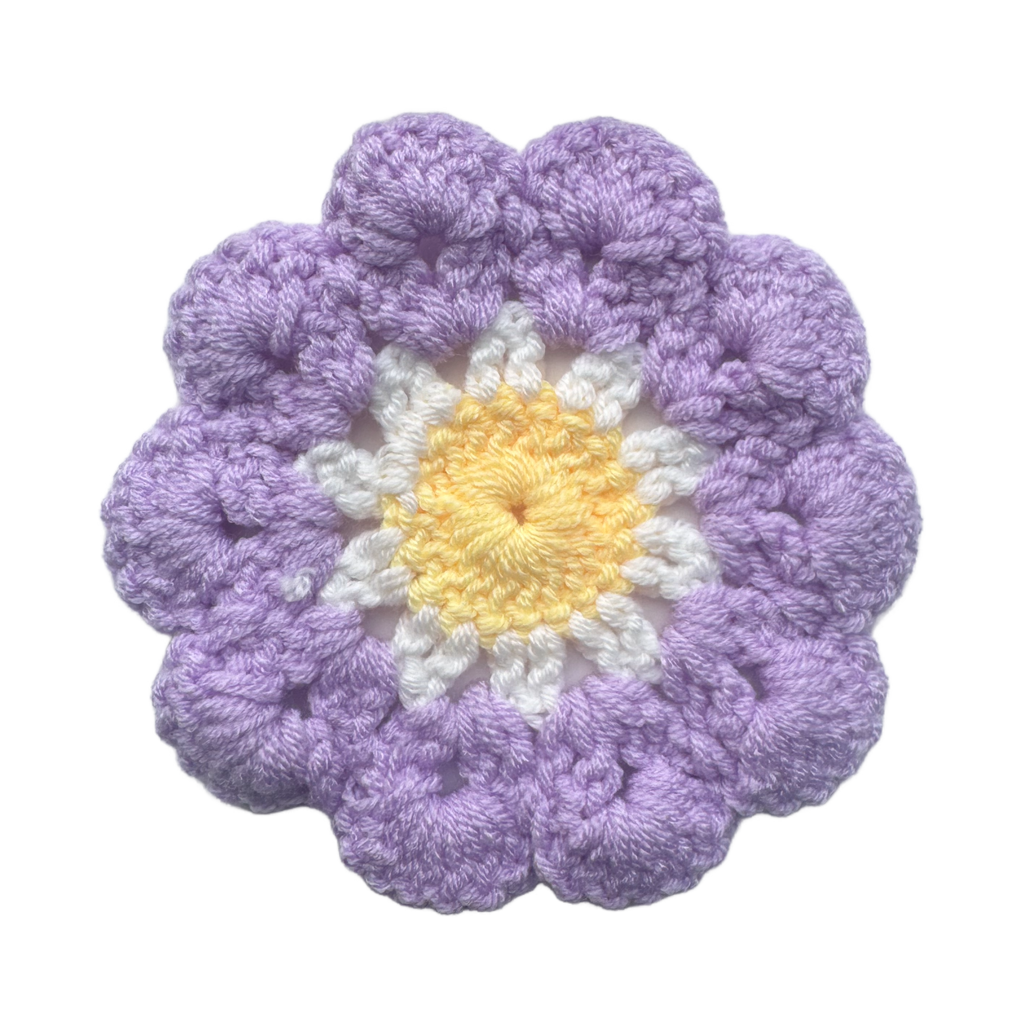 Crocheted flower with purple petals and a yellow center on a white background
