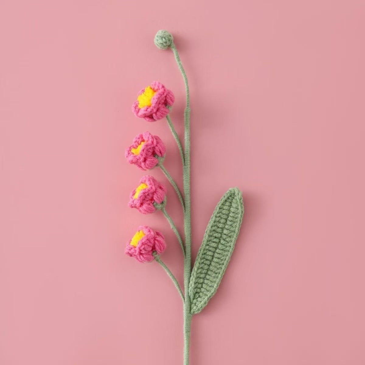 Crocheted Lily of the Valley puff flower with pink petals and yellow centers on a pink background