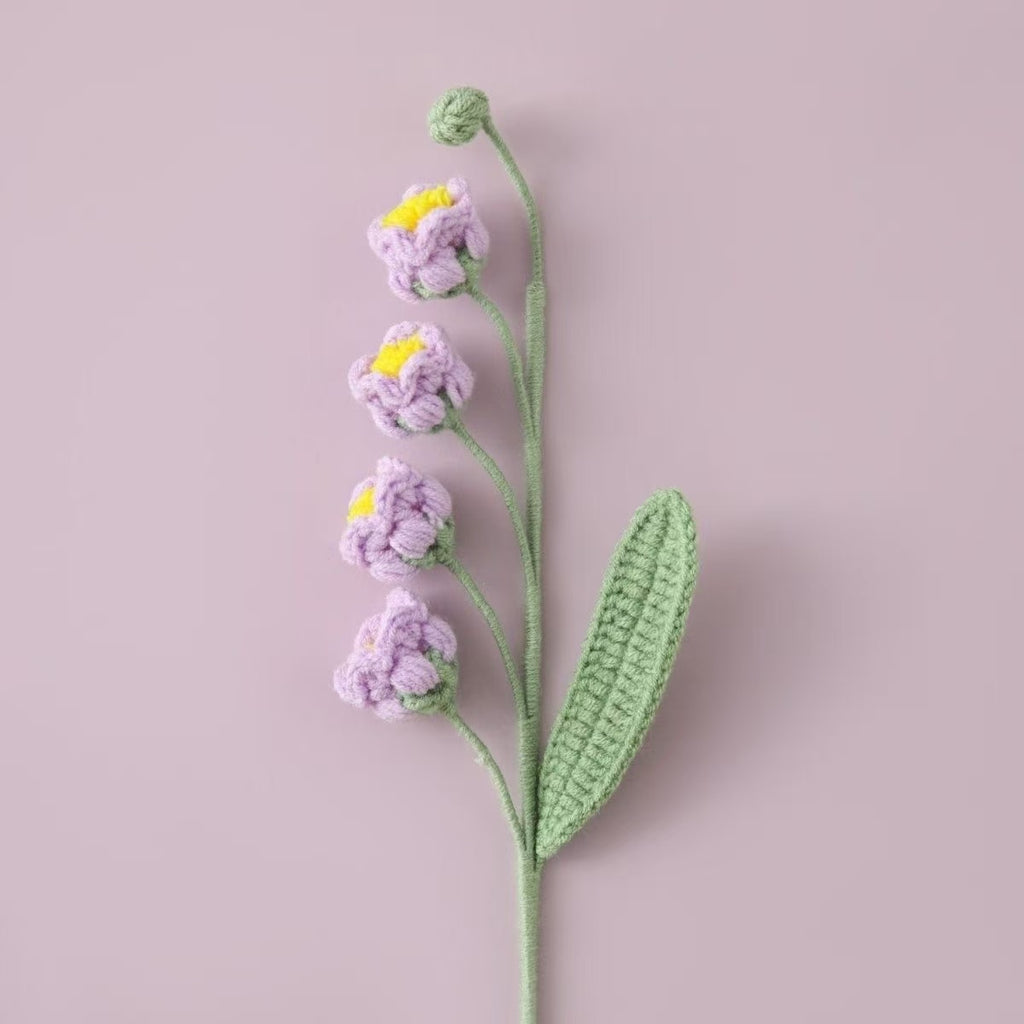Knitted Lily of the Valley puff flower with purple petals and green stem on a light pink background