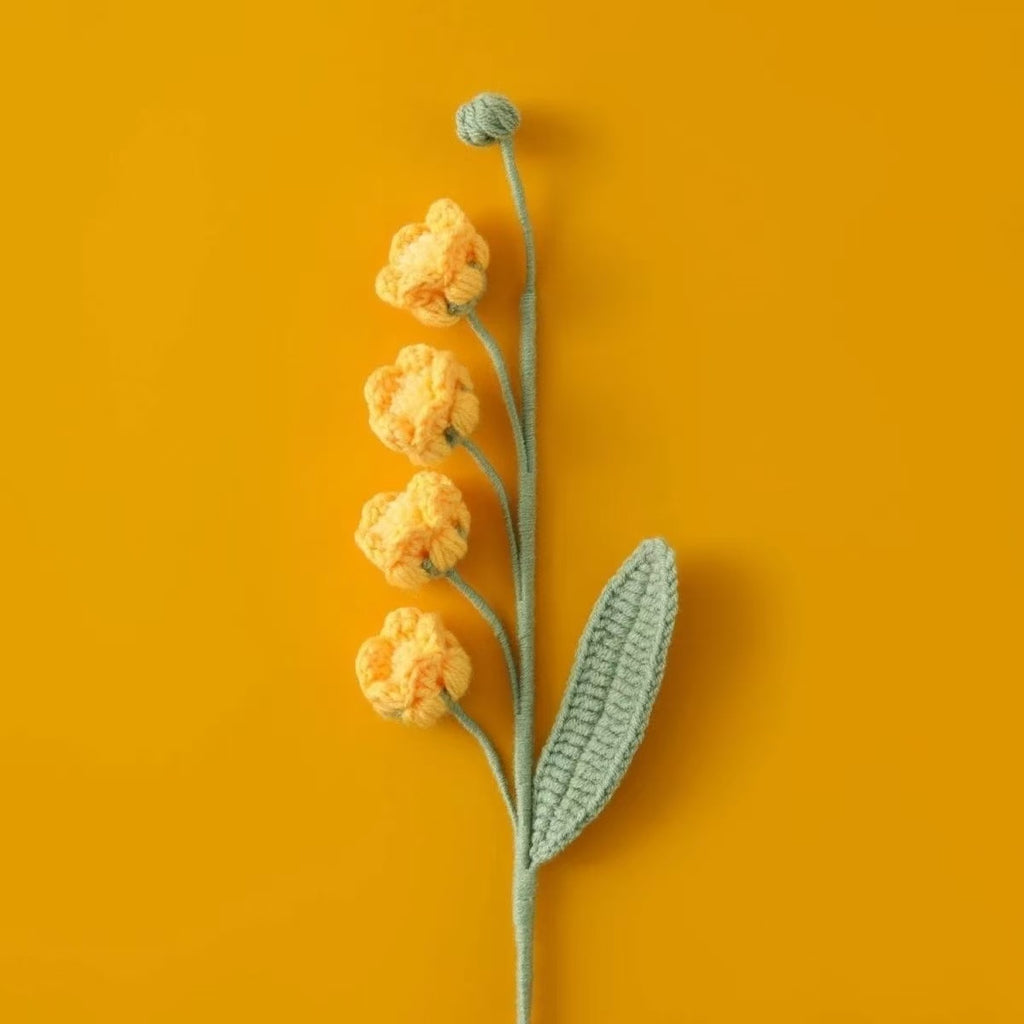 Knitted yellow Lily of the Valley puff flowers and green leaves on an orange background